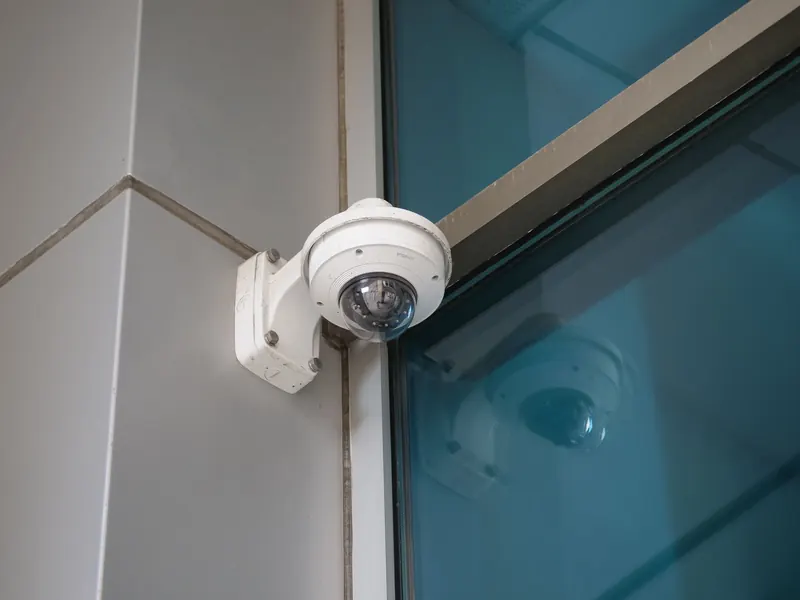 A white dome camera mounted against modern blue glazing