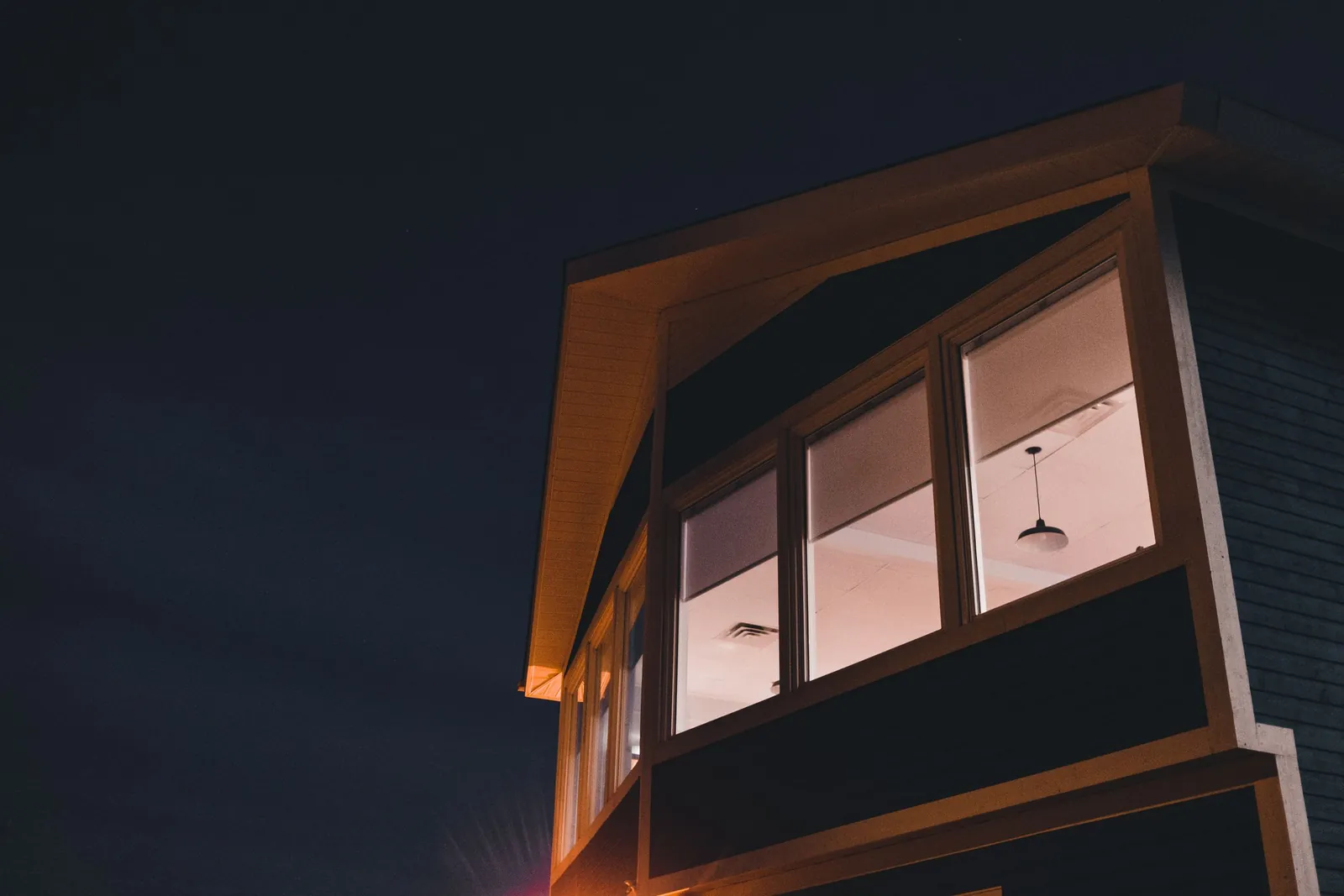 A modern home at night, its glass walls lit from within, seen from the dark garden