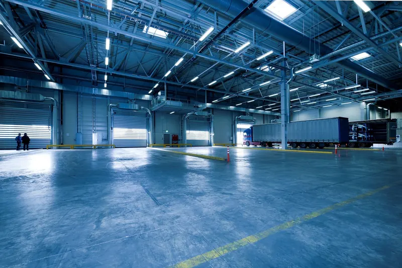 A large empty warehouse floor lit blue-white overhead